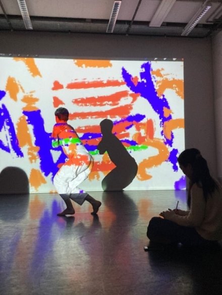 Patrick Wiel, student Dance Artist, danst op visuele aanwijzingen van Soyoon, die rechts in de hoek zit